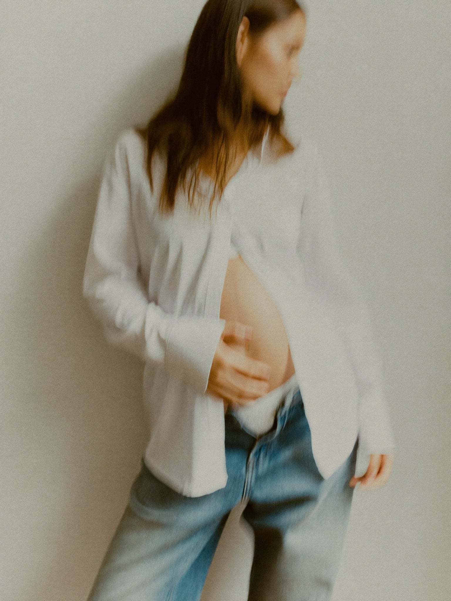 Blurry shot of pregnant woman in white shirt with unbuttoned jeans